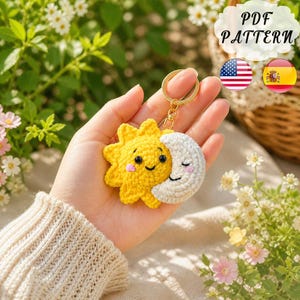Può includere: Un portachiavi all'uncinetto fatto a mano con un sole giallo e una luna bianca, entrambi con facce sorridenti e guance rosa. Il portachiavi ha un anello color oro. L'immagine include anche il testo "PDF PATTERN".