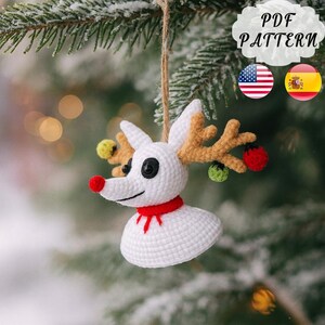 May include: A handmade white crochet reindeer Christmas ornament with a red nose, red scarf, and brown antlers. The ornament has black button eyes and is decorated with small colorful baubles. The text "PDF PATTERN" is visible.