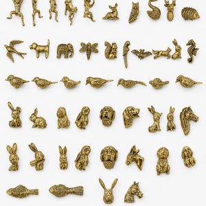 May include: A collection of antique gold-toned metal cabinet knobs and drawer pulls featuring various animal shapes including monkeys, birds, rabbits, dogs, horses, and insects. Each piece displays detailed textures and relief designs for furniture.