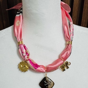 Pink silk scarf necklace with gold plated charms and a stone charm.