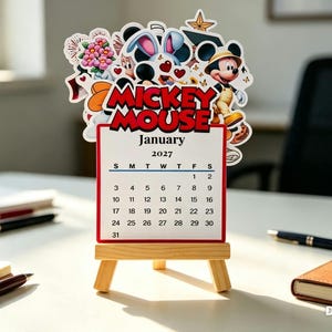 May include: A desktop calendar for January 2027 featuring a Mickey Mouse cutout topper with various character illustrations. The calendar is displayed on a small wooden easel stand, showcasing the month, year, and a grid of dates.