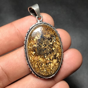 May include: Oval pendant with a silver-colored bail and a decorative silver-colored border. The pendant features a large, oval-shaped stone with a gold and brown pattern. The stone has a shiny, reflective surface.