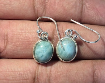 Pode incluir: Brincos de prata com pedras preciosas ovais azul claro. Os brincos têm um design simples com fecho de gancho. As pedras preciosas têm uma aparência marmoreada e a moldura de prata é polida.