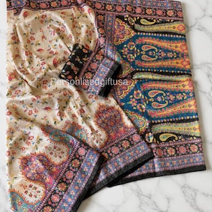 May include: A beige and floral patterned textile with a black border. The textile has a floral design in shades of red, pink, and green. The border features a paisley design in blue, yellow, and pink. The text "Personalisedgiftusa" is visible.