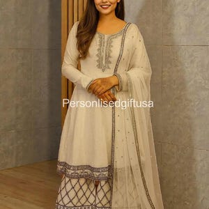Può includere: Completo salwar kameez color crema con ricami e abbellimenti intricati. La tunica a maniche lunghe presenta ricami argentati dettagliati intorno allo scollo e ai polsini. I pantaloni palazzo coordinati hanno un motivo geometrico. Il set include un dupatta trasparente. Testo sull'immagine: Personlisedgiftusa.