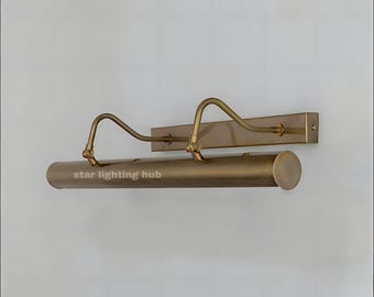 May include: A brass-colored picture light fixture with a rectangular backplate and a cylindrical light housing. Two curved arms extend from the backplate to the light housing. The text "star lighting hub" is printed on the light housing.
