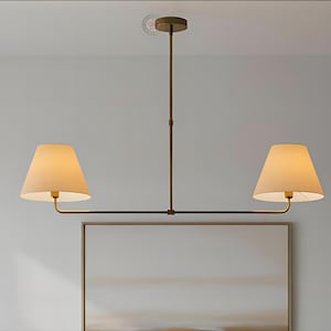 May include: A two-light pendant lamp in a bronze finish, featuring beige fabric shades. The lamp has a horizontal bar with two downward-facing shades and a vertical support rod. The shades are cone-shaped, and the fixture is ceiling-mounted.
