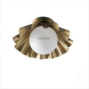 Può includere: Un lampadario da soffitto color ottone con un design a balze a forma di petalo che circonda un globo bianco. Il testo "star lighting hub" è stampato sul globo. Un elemento di illuminazione decorativo.
