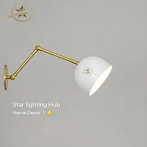 May include: A white, adjustable wall lamp with a gold-coloured arm and base. The lamp has a rounded shade and a star logo. The text "Star lighting Hub Home Decor" is also visible.