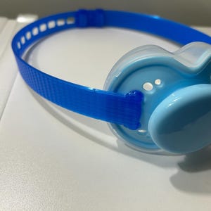 Peut inclure: Une sucette bleue avec une sangle bleue assortie. La sucette a une tétine bleu clair et un bouclier en plastique transparent. La sangle est en matériau tissé et comporte des trous espacés. Conçu pour les nourrissons.