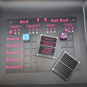 以下が含まれることがあります： ピンクのテキストとアクセントが付いた黒いゲームボード。ボードには「Bud」と「Not Bud」というラベルが付いたセクションがあり、ゲームラウンドを示すサイコロとテキストがあります。2つの黒いグリルと2つのサイコロも存在します。