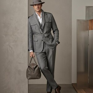 Elegant men’s grey three-piece safari-inspired suit styled with a scarf, hat, and leather travel bag.