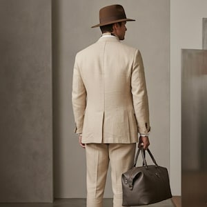 Men’s beige 3 piece suit in safari style with structured blazer, matching vest, formal pants, and leather travel bag.