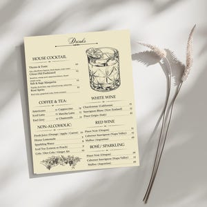 May include: A beige menu card with a detailed illustration of a cocktail glass. The menu lists house cocktails, coffee, tea, non-alcoholic drinks, white wine, red wine, and rosé/sparkling options. Dried plants are in the background.