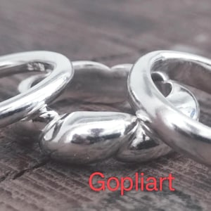 Peut inclure: Trois bagues en argent sont présentées sur une surface en bois. Les bagues ont une finition lisse et polie. La bague centrale a un design texturé unique, tandis que les deux autres sont des anneaux simples. Le mot "Gopliart" est écrit en rouge en bas.