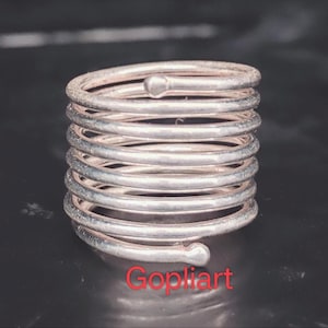 May include: A silver ring with a coiled design. The ring is made of multiple loops of metal, giving it a textured look. The word "Gopliart" is written in red at the bottom of the image.