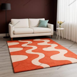 May include: An orange and cream-colored area rug with a wavy pattern. The rug is rectangular and placed on a light gray floor. A white sofa, a side table, and a floor lamp are in the background.