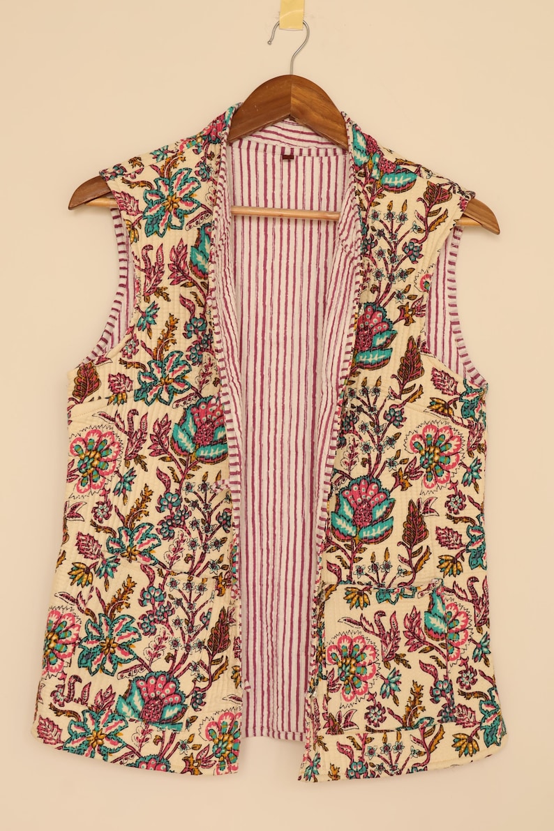 Puede incluir: Un chaleco sin mangas con estampado floral con fondo crema y un colorido estampado floral en tonos rosa, verde azulado y marr&oacute;n. El interior del chaleco presenta un estampado a rayas en blanco y burdeos. El chaleco est&aacute; colgado de una percha de madera.