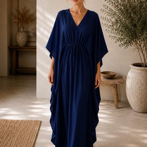 Peut inclure: Une robe caftan bleu marine longue jusqu'aux pieds avec un décolleté en V profond, des manches larges et fluides, et un cordon de serrage à la taille. Le vêtement est en tissu uni qui tombe souplement, créant une silhouette décontractée.
