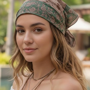 May include: A woman wearing a brown and green patterned headscarf. The headscarf has a floral design and is tied at the back of the head. She is also wearing a layered necklace.