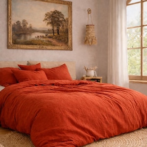 以下が含まれることがあります： 錆色の寝具と枕が置かれたベッドのある寝室。ベッドの上には大きな額入りの風景画が飾られています。ベッドの下には織りのラグがあり、壁には織りの壁掛けがあります。