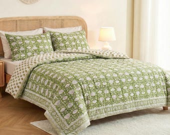 May include: A green and white floral patterned quilt set on a bed. The set includes a quilt and two pillowcases. The bed has a rattan headboard and a white rug at the foot of the bed. A lamp sits on the nightstand.