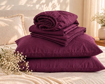 May include: A set of deep plum-colored bedding including two rectangular pillowcases and a folded flat sheet. The fabric has a visible, textured weave. The items are stacked neatly, showcasing the rich, dark purple hue of the textile material.