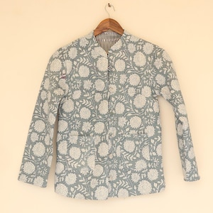 May include: A light blue jacket with a floral pattern in white. The jacket has a mandarin collar, long sleeves, and two front pockets. It is hanging on a wooden hanger against a light beige background. The interior lining is striped.