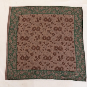 May include: A square, brown floral patterned textile with a green floral border. The center features a repeating pattern of brown flowers on a lighter brown background. The border is a darker green with floral and leaf designs.