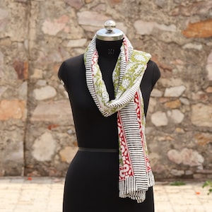 May include: A patterned scarf displayed on a black mannequin. The scarf features a design with white, black, red, and green elements. The scarf is draped around the mannequin's neck, showcasing its design and texture.