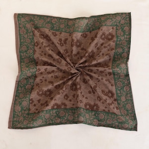 May include: A square scarf with a brown floral pattern and a green floral border. The scarf is folded and appears to be made of a soft fabric. The background is a plain white surface.