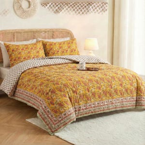 May include: A bed with a yellow floral patterned quilt and matching pillowcases. The quilt has a red and green border. The bed has a woven headboard and is in a well-lit room. A small wooden tray with a mug sits on the quilt.