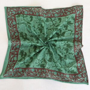 May include: A square, folded green scarf with a floral pattern. The scarf has a dark brown border with a repeating floral design. The center of the scarf is a lighter green with a darker green floral pattern.
