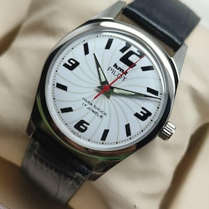 May include: Silver-toned wristwatch with a white face featuring black numerals and hands. The watch has a black leather band and a red second hand. The watch face has the text "hmt PILOT" and "PARA SHOCK 17 JEWELS INDIA".