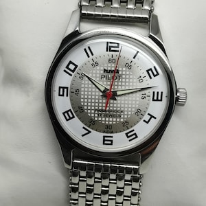 May include: Silver wristwatch with a white face and black numerals. The watch face features the word "PILOT" and "PARA SHOCK 17 JEWELS INDIA". The watch has a silver-toned strap.