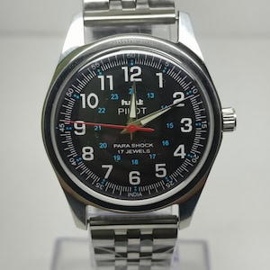 May include: A silver wristwatch with a black face. The watch features white numerals, a red second hand, and the text "PILOT" and "PARA SHOCK 17 JEWELS". The watch has a silver metal band.