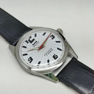 May include: A silver-toned wristwatch with a white face featuring black numerals and a red second hand. The watch has a black leather band. The watch face has the text "hmt PILOT PARA SHOCK 17 JEWELS INDIA".