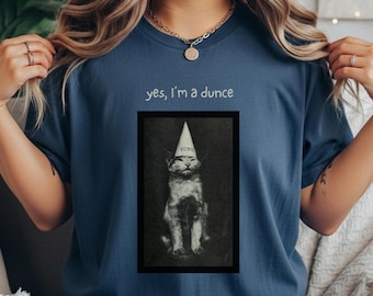May include: A navy blue t-shirt with the text "yes, I'm a dunce" above a framed black and white image of a cat wearing a dunce cap. The cat image has the word "dunce" on the cap.