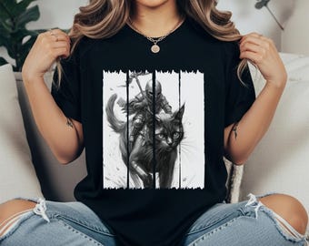 May include: Black t-shirt featuring a black and white graphic of a knight riding a cat. The knight is armored and holding a weapon. The cat has a determined expression. The design is framed by vertical white stripes.