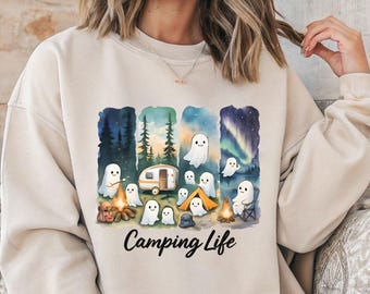 May include: Beige sweatshirt featuring a watercolor illustration of ghosts camping. The design includes a camper, campfire, tent, and forest scenes. The words "Camping Life" are written in a script font below the illustration.