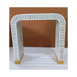 May include: A white and gray striped side table with a U-shaped design. The table has a rectangular top and base with a gold-colored trim. The gray stripes are vertical and evenly spaced.