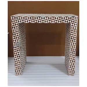 May include: A rectangular console table with a geometric pattern. The table is constructed with a mosaic of brown and white triangular pieces. The table has a flat top and two open sides, with a height of approximately 30 inches.
