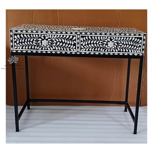 May include: A black and white floral patterned console table with two drawers. The table has a black metal frame and legs. The drawers feature a floral design with white accents. The table is a decorative furniture piece.