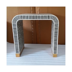 May include: A modern side table with a unique U-shaped design. The table features a black and white striped pattern on the top and sides, with gold-colored accents on the feet. This decorative table is a stylish addition to any living space.