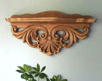 Può includere: Mensola da parete decorativa in legno con dettagli intagliati ornati. La mensola è di un caldo colore marrone dorato e presenta un bordo superiore smerlato e un'intricata lavorazione a volute. La mensola è larga circa 61 cm.
