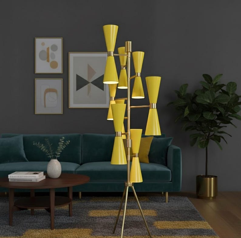 May include: A tall, yellow floor lamp with a brass frame. The lamp has multiple cone-shaped shades and stands on a tripod base. The lamp is in a living room with a teal sofa, a round wooden coffee table, and framed artwork on the wall.