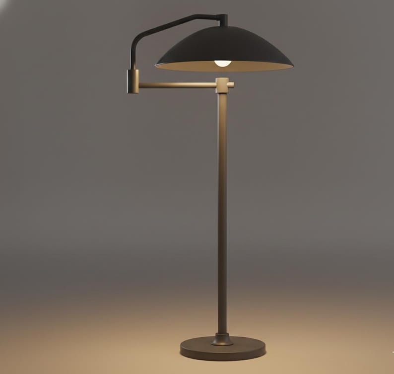May include: A contemporary floor lamp featuring a black lampshade with a gold interior. The lamp has a bronze-coloured adjustable arm and a circular base. The light is on, illuminating the lampshade's interior.
