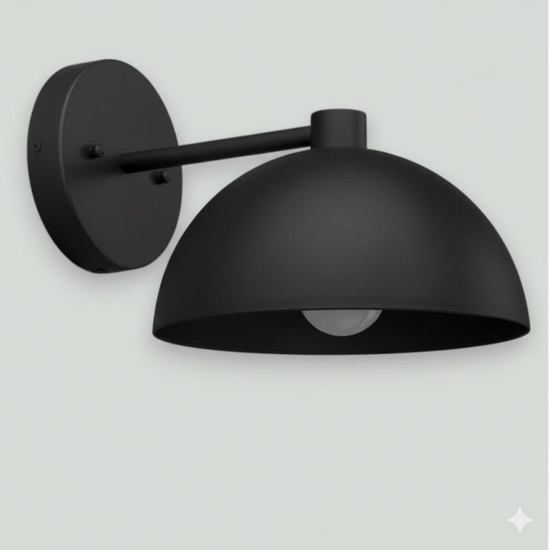 May include: A black wall-mounted light fixture with a dome-shaped shade. The fixture has a circular base and a straight arm connecting to the shade. The light bulb is visible inside the shade.