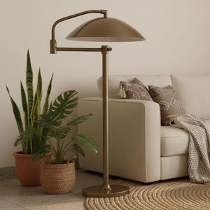 May include: A bronze floor lamp with a curved arm and a domed shade. The lamp is positioned beside a beige sofa with decorative cushions and a woven throw. Potted plants in terracotta and woven baskets are also in the image.