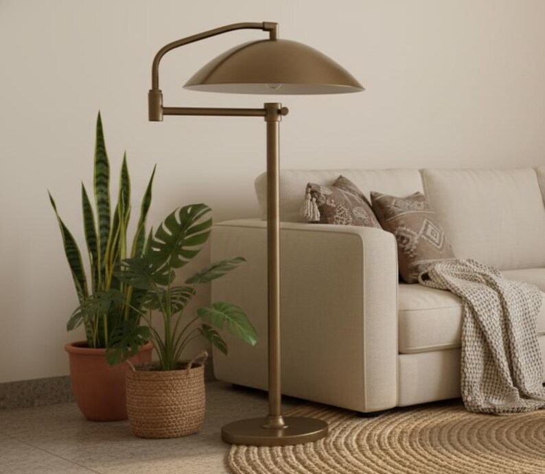 May include: A bronze floor lamp with a curved arm and a domed shade. The lamp is positioned beside a beige sofa with decorative cushions and a woven throw. Potted plants in terracotta and woven baskets are also in the image.